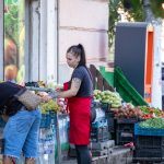 Фотография продавца на рынке с татуировкой на руке и покупателем. Виден фрагмент черно-серого рисунка татуировки на предплечье.