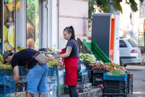 Фотография продавца на рынке с татуировкой на руке и покупателем. Виден фрагмент черно-серого рисунка татуировки на предплечье.