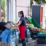 Фотография продавца на рынке с татуировкой на руке и покупателем. Виден фрагмент черно-серого рисунка татуировки на предплечье.
