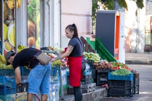 Фотография продавца на рынке с татуировкой на руке и покупателем. Виден фрагмент черно-серого рисунка татуировки на предплечье.