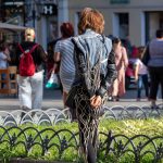 Фотография уличной татуировки на спине девушки в джинсовой куртке, демонстрирующая сложный геометрический рисунок в стиле стрит-арт.