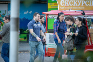 Фотография мужчины с татуировкой на руке, одетого в джинсовую рубашку и джинсы, идущего по улице.