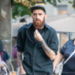 Фото тату: мужчина с длинной бородой и татуировками на предплечьях, выполненными в черно-серых тонах, демонстрирует свои татуировки.