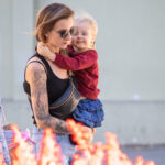Фото тату: молодая женщина держит ребенка, на ее предплечье видна татуировка с изображением лебедя, выполненная в черно-серых тонах.