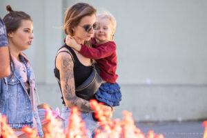 Фото тату: молодая женщина держит ребенка, на ее предплечье видна татуировка с изображением лебедя, выполненная в черно-серых тонах.