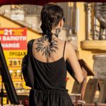 Фотография татуировки на спине девушки, выполненной в черных тонах. Изображен стилизованный растительный орнамент, напоминающий ветви дерева.
