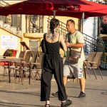 Фотография уличной татуировки на девушке, идущей по городской улице. Видна татуировка на спине и шее, выполненная в темных тонах.