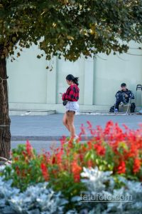 Фотография девушки, идущей по улице с видимой татуировкой на бедре. Она одета в шорты и клетчатую рубашку.