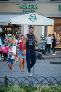 Фотография мужчины, идущего по улице с видимой татуировкой на плече. Он одет в майку и спортивные штаны.