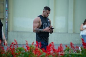 Фотография мужчины с татуировкой на руке, смотрящего в телефон. На заднем плане видны люди и цветы.