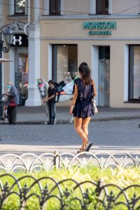 Фотография женщины, идущей по улице с видимой татуировкой на внутренней стороне предплечья. Татуировка выполнена в темных тонах и имеет растительный мотив.