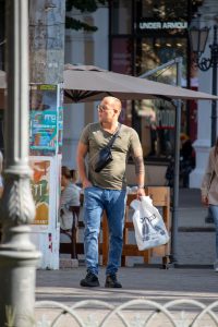 Фотография мужчины, идущего по улице с полинезийской татуировкой на правой руке. Мужчина одет в повседневную одежду и несет пакет.