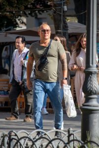 Фотография мужчины, идущего по улице с заметной татуировкой в полинезийском стиле на правой руке. Мужчина одет в повседневную одежду и несет пакет.