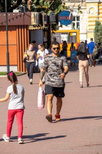 Фотография мужчины с татуировкой на руке, идущего по улице. Татуировка выполнена в ярком стиле, заметна на фоне повседневной одежды.