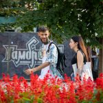 Фотография пары на улице с видимыми татуировками на руках. Мужчина в яркой рубашке, девушка в черном топе.