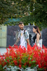 Фотография пары с татуировками на руках, гуляющей по парку. Мужчина и женщина смотрят друг на друга, демонстрируя свои татуировки.