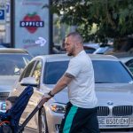 Фото мужчины с татуировкой на предплечье, толкающего детскую коляску по улице. Видна часть рисунка татуировки на открытой коже.