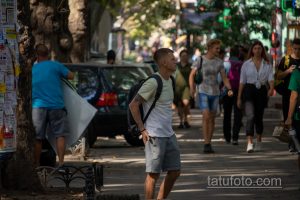 Фото тату на спине мужчины, идущего по улице. Виден небольшой рисунок татуировки на открытой коже, когда рубашка приподнята.