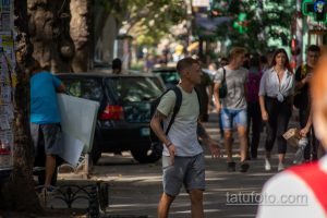 Фото татуировок на руках мужчины, идущего по улице. Видны рукава с татуировками, повседневная одежда, городская обстановка.
