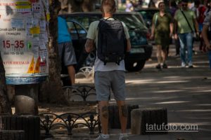 Фото татуировок на руках мужчины с рюкзаком. Видны рукава с татуировками, повседневная одежда, городская обстановка.