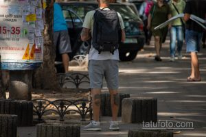 Фото татуировок на руках мужчины с рюкзаком. Видны рукава с татуировками, повседневная одежда, городская обстановка.