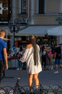 Фотография татуировки на плече женщины, вид сзади. Видна часть рисунка татуировки, выполненной в черном цвете. Женщина едет на электросамокате.