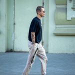 Фотография мужчины, идущего по улице с яркой татуировкой на руке в японском стиле. Детализированный рисунок с использованием ярких цветов.