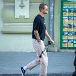 Фотография мужчины, идущего по улице с яркой татуировкой на руке в японском стиле. Детализированный рисунок на фоне городской архитектуры.