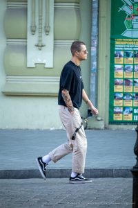 Фотография мужчины, идущего по улице с яркой татуировкой на руке в японском стиле. Детализированный рисунок на фоне городской архитектуры.