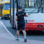 Фото мужчины с татуировками на голени, стоящего возле автобуса. Татуировки в стиле олдскул с черепами, розами и птицами.