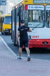 Фото мужчины с татуировками на голени, стоящего возле автобуса. Татуировки в стиле олдскул с черепами, розами и птицами.