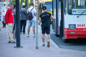 Фото мужчины с татуировками на голени и руке. Вид сбоку, мужчина идет по улице рядом с трамваем. Татуировки в стиле олдскул.