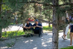 Фотография двух полицейских, сидящих под деревом и смотрящих в телефоны. На предплечьях видны татуировки с надписями.