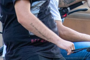 Фото тату на руке мужчины с надписью, выполненной черными чернилами. Надпись выглядит как цитата или личное послание. Уличная фотография.