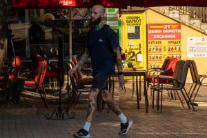 Фото тату на руках и ногах мужчины, идущего по улице. Татуировки выполнены в черном цвете и представляют собой сложные узоры и рисунки. Уличная фотография.