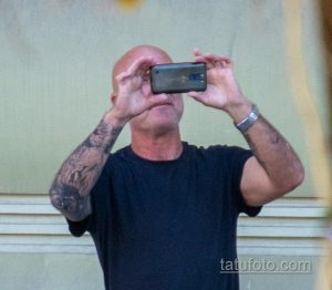 Фото мужчины с татуировкой на руке, держащего телефон. Видна детализированная татуировка на предплечье.