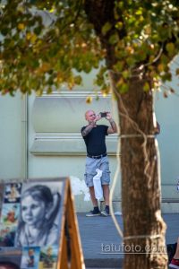 Фото мужчины с татуировкой на руке, фотографирующего на телефон. Видна детализированная татуировка на предплечье.