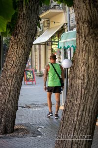 Фото тату на руке мужчины, идущего по городской улице. Видна детализированная татуировка, покрывающая большую часть руки.