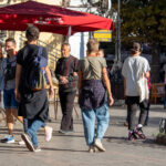 Фотография женщины, идущей по улице с татуировкой на руке. Татуировка выполнена в темных тонах и выглядит минималистично.