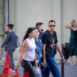 Фотография уличной татуировки на предплечье женщины, идущей по улице с друзьями. Татуировка выполнена в темных тонах и выглядит минималистично.