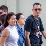Фото девушки с татуировкой на руке, идущей по улице в компании других людей. Рисунок татуировки выполнен в технике тонкой линии, изображает цветочный орнамент.