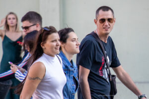 Фото девушки с татуировкой на руке, идущей по улице в компании других людей. Рисунок татуировки выполнен в технике тонкой линии, изображает цветочный орнамент.