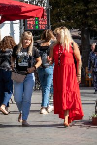 Фотография двух женщин на улице, одна из которых в красном платье, демонстрирует татуировку тигра на руке.