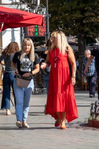 Фотография двух женщин на улице, одна из которых в футболке с изображением тигра, демонстрирующей татуировку на плече.