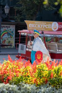 Фотография уличного тату-перформанса в Одессе. Мужчина в ярком костюме и с татуировкой на руке демонстрирует искусство татуировки на фоне туристического автобуса.