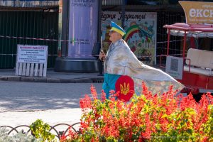 Фотография уличного художника в серебристой накидке и желтых брюках с украинским флагом, идущего по улице в Одессе.
