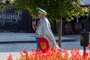 Фотография уличного художника в серебристой накидке и желтых брюках с украинским флагом, стоящего на улице в Одессе.