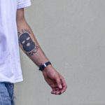 Фото татуировки на руке: изображение маски в стиле граффити. Черно-белая татуировка, выполненная в реалистичном стиле. Крупный план.