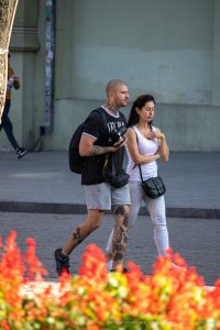 Фото мужчины с татуировками на руках и ногах, идущего по улице с девушкой. Видны детализированные рисунки в различных стилях.