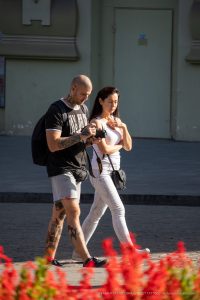 Фото мужчины с множеством татуировок на ногах и руках, идущего по улице с девушкой. Разнообразные рисунки, включая традиционные и современные стили.